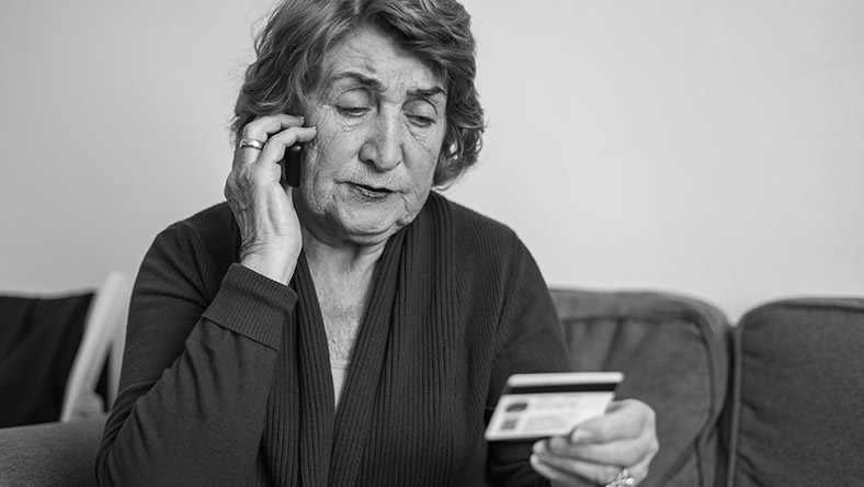 A woman reads her bank card while using the phone.