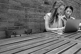 Two women sitting outdoors looking at laptop