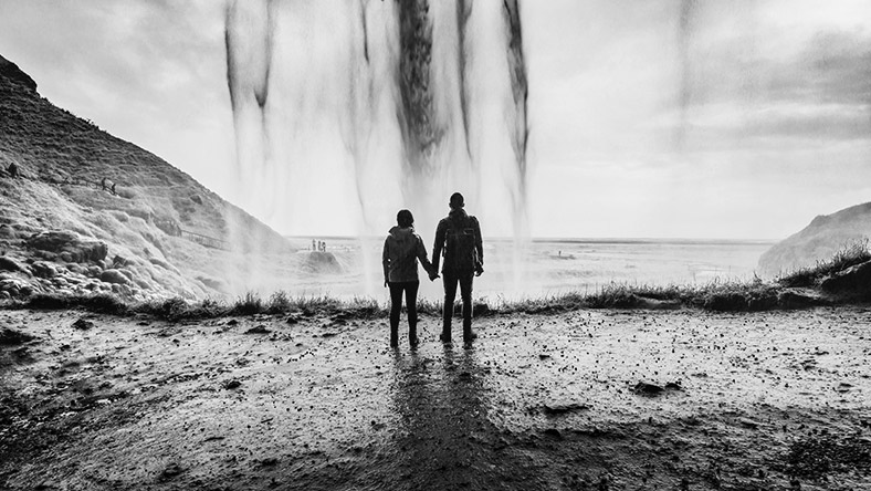 Silhouette of two people holding hands looking out over a large body of water.