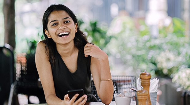 A smiling woman in a cafe while banking on her phone.