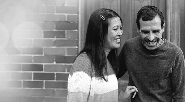 A young man and woman hold each other in a living room and smile happily. The man is holding the keys to their first home.