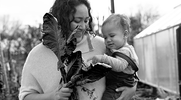 A woman holds a child and is showing them homegrown broccoli.