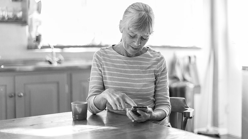A woman sits at her kitchen table using her mobile phone.