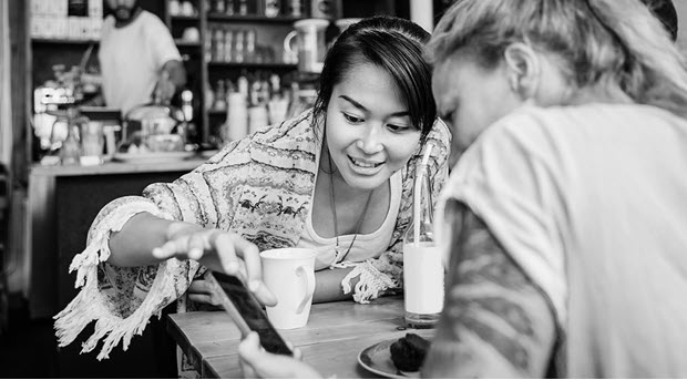 Two friends sitting in a a cafe looking at a mobile phone.