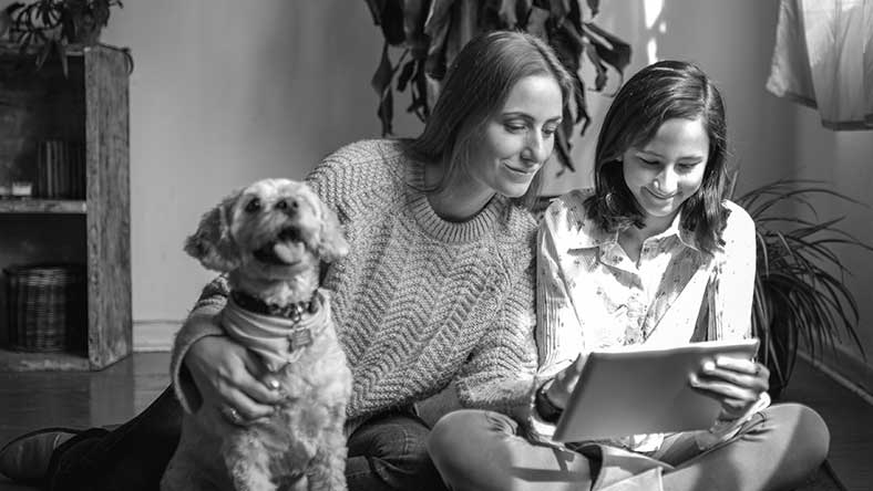 Two women looking at ipad and smiling with dog by side