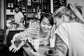 Two female friends using a smartphone to transfer money while out for coffee.