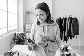 A woman looking at a phone in her right hand while holding a mug in her other hand.