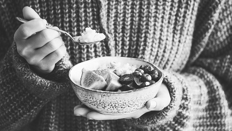 Close shot of a woman holding a bowl of fruit, eating it with a spoon.