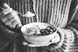 Close shot of a woman holding a bowl of fruit, eating it with a spoon.