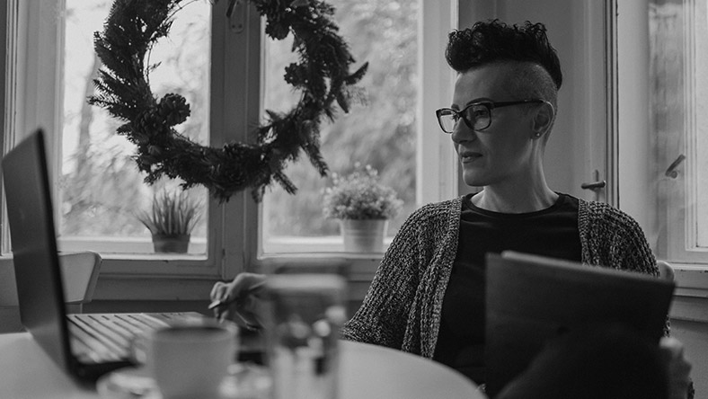 A young woman sits at her kitchen table shopping on her laptop