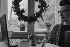 A young woman sits at her kitchen table shopping on her laptop