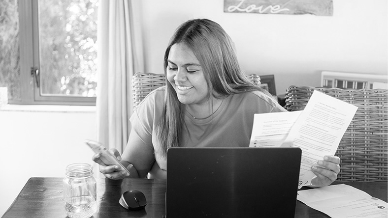 A young woman uses using her phone, laptop and documents to assess if a personal loan or an overdraft is right for her,