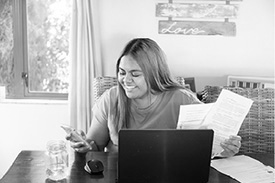 A young woman uses using her phone, laptop and documents to assess if a personal loan or an overdraft is right for her,