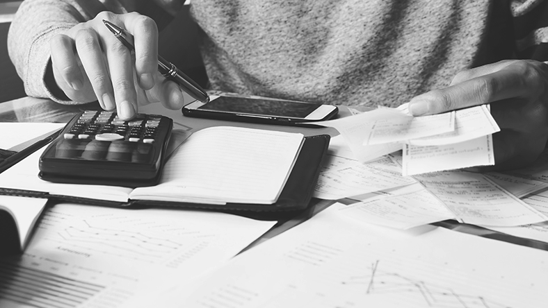 Black and white image of a person using a calculator, cropped to show just the calculator, hands and torso.