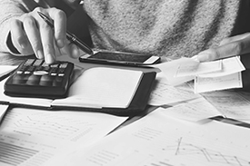 Black and white image of a person using a calculator, cropped to show just the calculator, hands and torso.