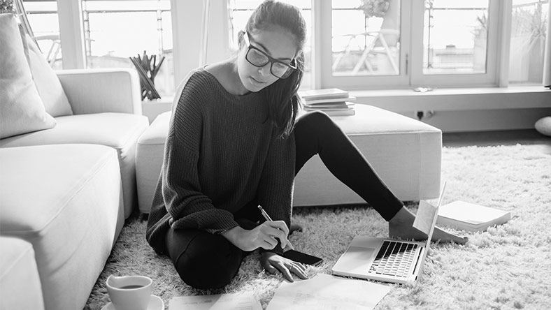A woman sitting on the floor with her laptop, phone and notebook working out her budget to take control of her finances with a personal loan.