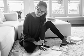 A woman sitting on the floor with her laptop, phone and notebook working out her budget to take control of her finances with a personal loan.