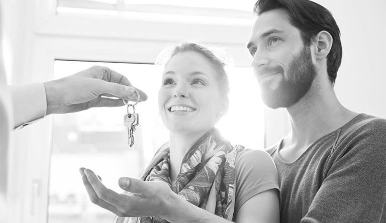 Young couple holding out hand to receive keys to new home