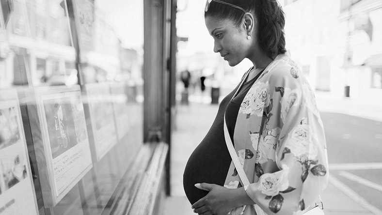 An expectant mother looking at house listings on a real estate's window.