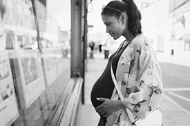 An expectant mother looking at house listings on a real estate's window.