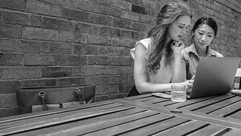 Two women sitting outdoors looking at laptop