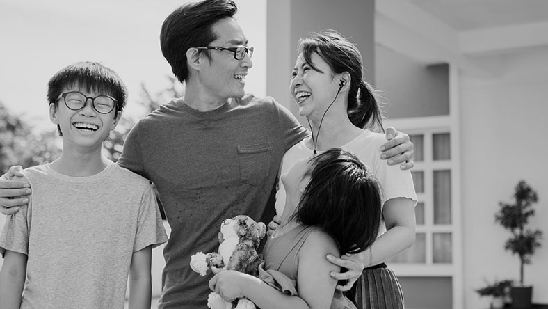 Parents stand and smile with their two children outside their new home.