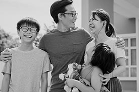 Parents stand and smile with their two children outside their new home.