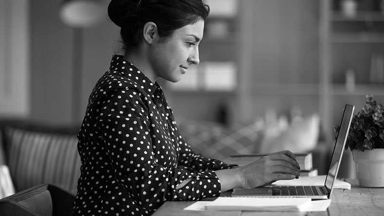 A young woman types on her laptop from her living room.