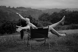 A black and white photo of a woman relaxing in a chair in an open field.