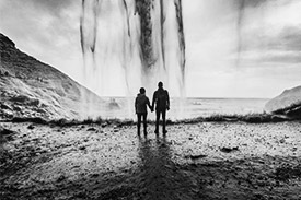 Silhouette of two people holding hands looking out over a large body of water.