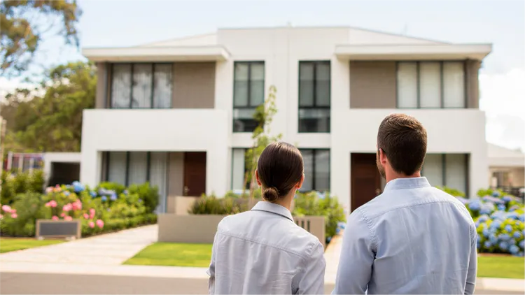 A man and woman stand together facing a modern white duplex-style house.